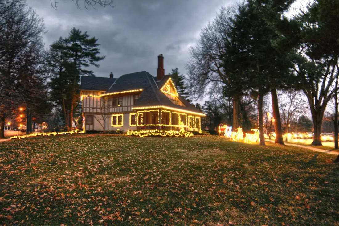 A Tudor-style home outlined in Christmas lights near Ward Parkway at dusk